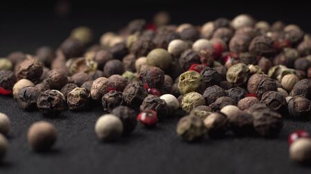 Mixed peppercorns falling on black table in kitchen with black background