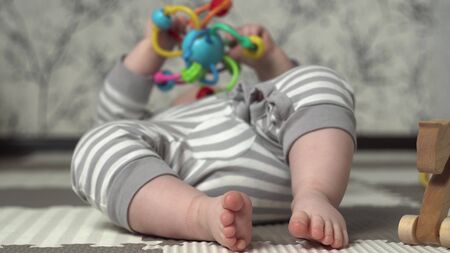 Baby feet in the frame. The kid in striped pajamas is played with a childrens colored toy on the floor.の写真素材