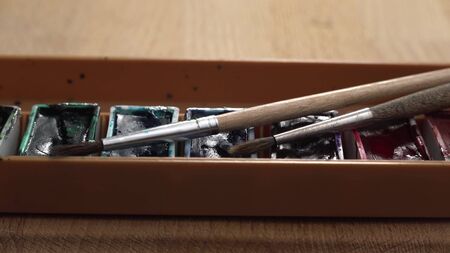 Dolly footage of palette with gouache lies on a wooden table. Different colors of paint on this...