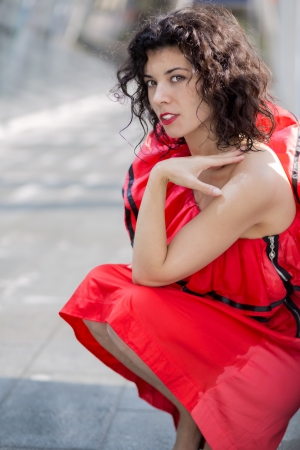 Woman in red dress squatting at sunny squareの写真素材