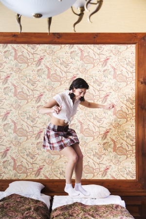 Woman in schoolgirl dress jump on wide bedの写真素材