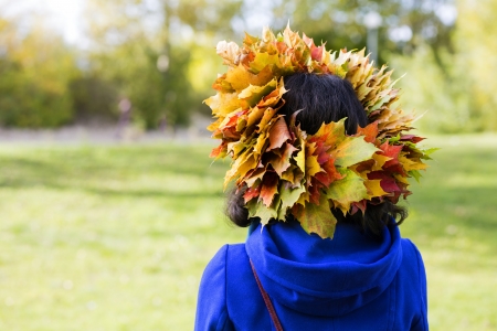Woman with maple leaves on head from behindの写真素材