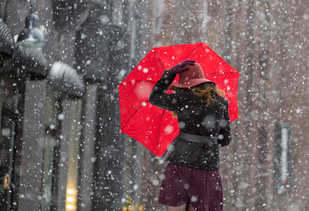 Woman try hold hat and umbrella from behindの写真素材