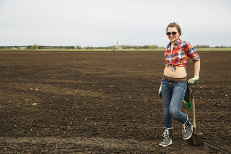 Young woman with sharp shovel and cultivated fieldの写真素材