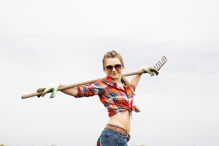 Young woman with rake on gray cloudy backgroundの写真素材