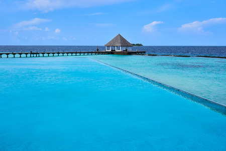 View of wooden path leading to bungalow style deck on turquoise ocean of the Coco Bodu Hithi resort in Maldives seen from the infinity swimming pool.の写真素材