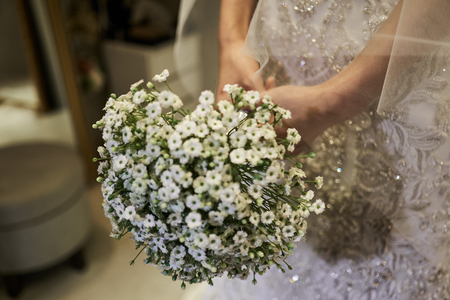 Bride in white dress with veil gently covering her arms holding a white bouquet.の写真素材