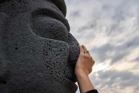Woman's hand touching the nose of harubang sculture at a park near the ocean of Jeju Island, South Korea.の写真素材
