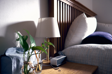 Bedroom with pillows, lamp. tissue box, vase, defuser, and portable speake lit with warm sun lightの写真素材