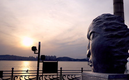A large head shaped statue facing the sunset ocean in a public park at Yongin, South Korea.