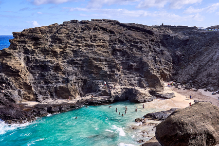 Many people enjoying the waves and the ocean at a secluded beach surrounded by rocky cliffs.の写真素材