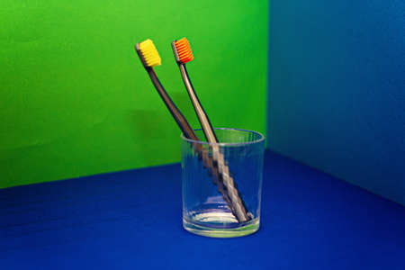 Two selective focus toothbrushes in a transparent glass on a colored backgroundの写真素材