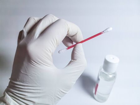 A hand in a white rubber glove holds a cotton swab against the background of a small bottle with an antiseptic. Image with selective focusの写真素材