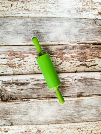 Kitchen utensils. Bright green rolling pin on background with aged wooden boards.