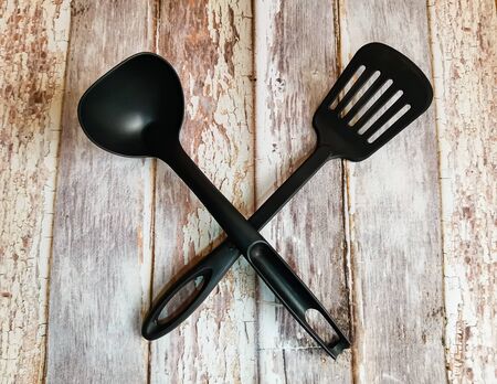 Kitchen utensils. Black plastic kitchen spatula and ladle on background with aged wooden boards.の写真素材