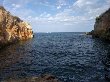 A narrow bay between two high cliffs. View to the horizon, deep blue sea and blue sky on the island of Mallorca, Spain. In the background, yachts are visible. Traveling concept background.の写真素材