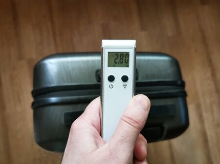 White electronic scales for luggage in a hand. The picture shows the weighing of hand luggage and luggage before traveling.の写真素材