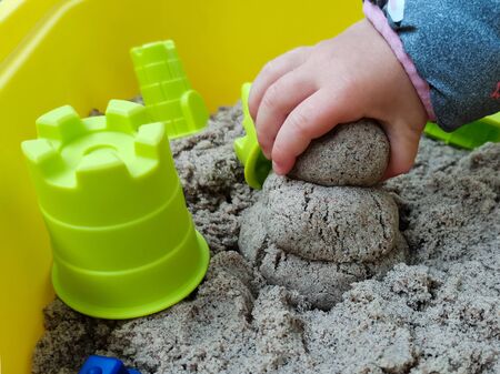 The child makes of a sandyman from kinetic sand. Pictured is a child's hand holding sand and plastic kinetic sand toys. Kinetic sand is a natural color. Image with selective focus.の写真素材