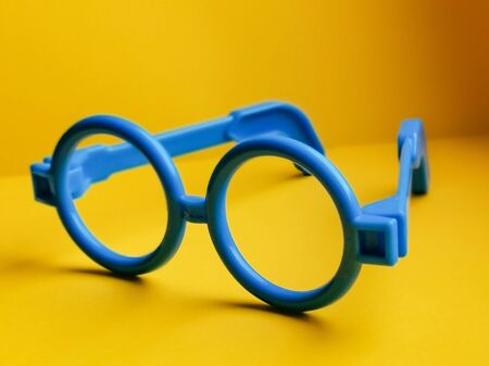 Blue plastic toy glasses for kids on yellow background. For playing a doctor, scientist or teacher. Image with selective focus.の写真素材