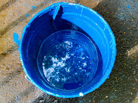 A bucket with bright blue paint in which the sky and tree branches are reflected. Concept: beauty is everywhere. Painting works.の写真素材