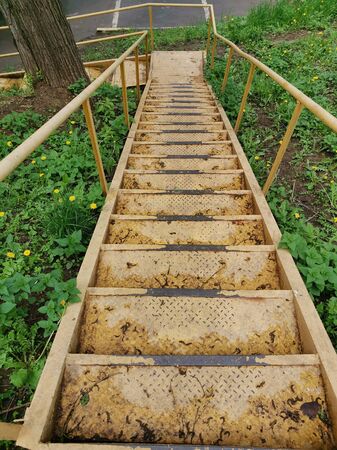 Old shabby metal staircase in yellow. Uneven steps. Unfriendly urban environment for the disabled.の写真素材