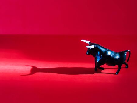 Close-up of a black bull figurine in the sun on a red background. Expressive shadow with horns. Symbol of 2021.の写真素材