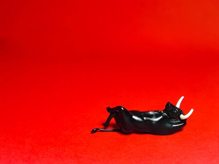 Close-up of a black bull figurine on a red background. The bull is imposingly lying on its back. A pose of relaxation and rest. Symbol chinese lunar horoscope 2021の写真素材