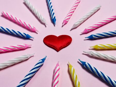 Birthday candles and red heart in the center on a pink background. Greeting card or birthday background. Romantic picture for the wedding anniversary and Valentine's Day.の写真素材