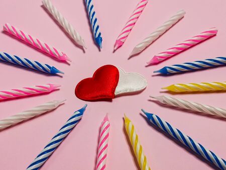 Birthday candles and two hearts in the center on a pink background. Greeting card or birthday background. Romantic picture on the wedding anniversary.の写真素材
