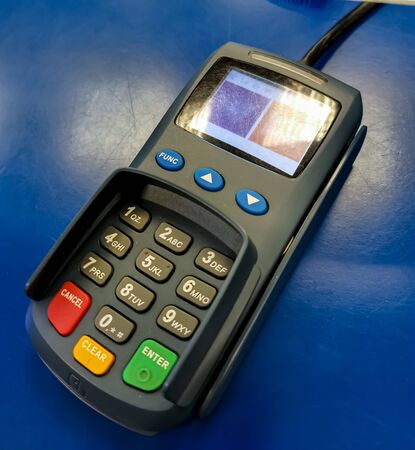 Bank card payment terminal. Old plastic card terminal with scuffs and scratches on a blue shabby background. Frequent use of the terminal. Cashless settlement.の写真素材