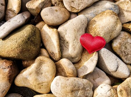 Closeup of a red heart on round stones in the rays of the sun. Background for design or screensaver, place for your text. Selective focus image on red heart.の写真素材