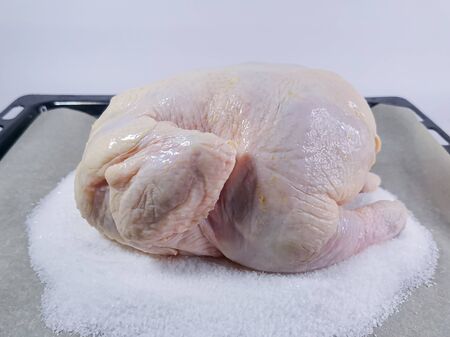 Raw chicken carcass is waiting for cooking on a baking sheet. Chicken is laid on coarse salt and baking parchment. Home kitchen. Quick and easy recipeの写真素材