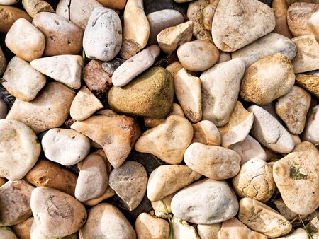 Texture of round stones in beige tones. Abstract background with round peeble stones for designers. Top view in the sunlight.の写真素材