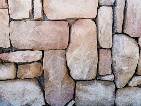The texture of large stones in beige tones. Abstract stone wall background for designers. Front view in the sunlight.の写真素材