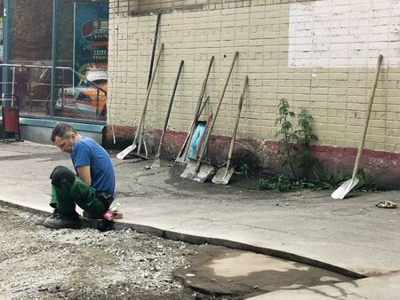 Moscow / Russia - 06/06/2020: Tired janitor resting, sitting on the pavement. social problem: low-paid labor in the municipal sector. Violation of the rights of of guest worker.の写真素材