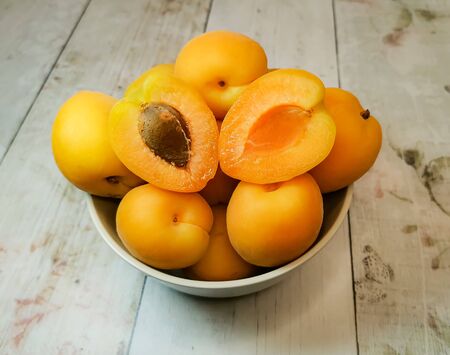 Close-up of fresh juicy apricots in a deep plate, one of which is cut in half on a wooden tabletop. Concept: fresh seasonal fruits, the comfort of a country house, fruits from my garden.の写真素材