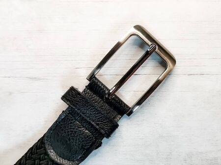Close-up of a silver buckle from a trouser belt on a wooden tabletop background. Accessories and elements of everyday style in clothes.の写真素材
