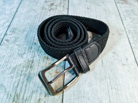 Black wicker trouser belt with a silver buckle on a wooden tabletop background. Rolled up trouser belt close-up. Accessories and elements of casual style of dress.の写真素材