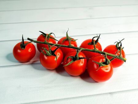 Fresh ripe cherry tomatoes on a green branch on a background of light wooden boards. Horizontal position, side view. Useful seasonal vegetables, a source of vitamins and minerals. Healthy diet.の写真素材