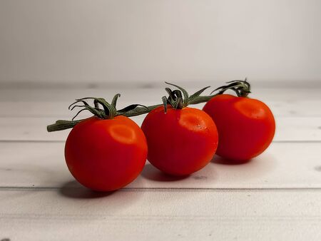 Fresh ripe cherry tomatoes on a green branch on a background of light wooden boards. Horizontal position, side view. Useful seasonal vegetables, a source of vitamins and minerals. Healthy diet.の写真素材