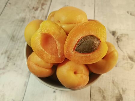 Close-up of fresh juicy apricots in a deep plate, one of which is cut in half on a wooden tabletop. Concept: fresh seasonal fruits, the comfort of a country house, fruits from my garden.の写真素材