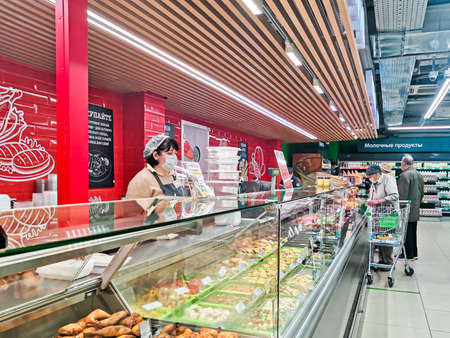 Moscow / Russia - 06.06.2020: Customers and seller behind the counter with ready-made meals of a large supermarket  in a mask and gloves. Mandatory measures to prevent the spread of the virus.のeditorial素材