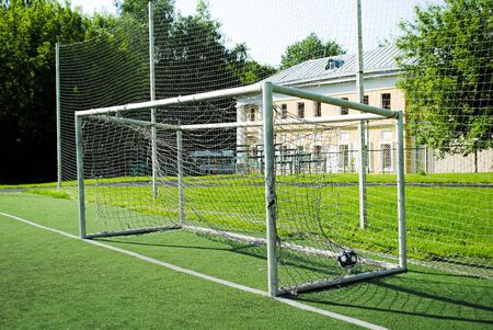 A ball in a soccer goal on an amateur soccer field on a sunny summer day. Gates with a torn and dirty net. Sports group games on a professional and amateur level. Summer outdoor sports.の写真素材