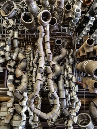 Bent pieces of rusted metal pipes hanging garland in a metal workshop. Steel welding fittings, elbows. Locksmith and plumbing tools and repair parts.の写真素材
