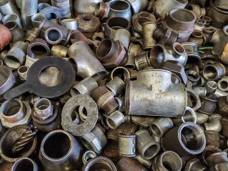 Bent pieces of rusted metal pipes and other metal parts in a metal workshop. Steel welding fittings, elbows. Locksmith and plumbing tools and repair parts.の写真素材