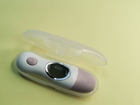 White electronic non-contact thermometer for measuring body temperature in children and adults on pale yellow background. The device is in individual transparent plastic case. Modern medical devicesの写真素材