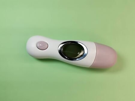 White electronic non-contact thermometer for measuring body temperature in children and adults on a light-green background. Safe, modern medical devicesの写真素材