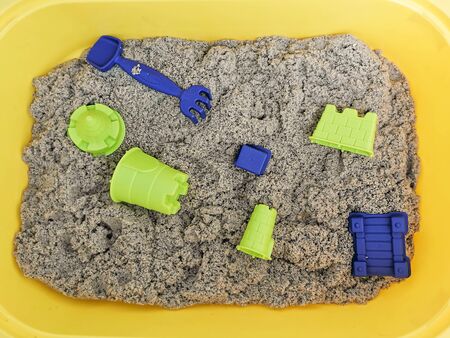 Kinetic sand of natural color with toys in a yellow container. Educational games with children for fine motor skills.の写真素材