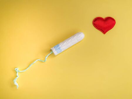 Cotton tampon and red heart on yellow background. Concept: women's health care, intimate hygiene, gynecological menstruation cycle. Flat layout, top view.の写真素材