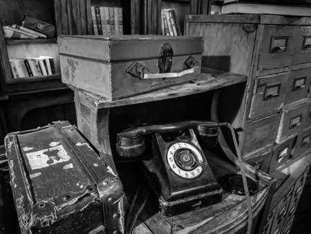 Moscow / Russia - 07.16.2020: Old rotary dial telephone, suitcase and books on the background of bookcases in a vintage interior. Black and white image.のeditorial素材